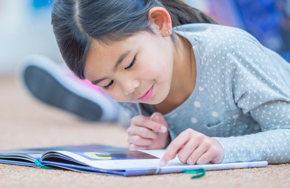 A young child reading a book while laying on the floor.